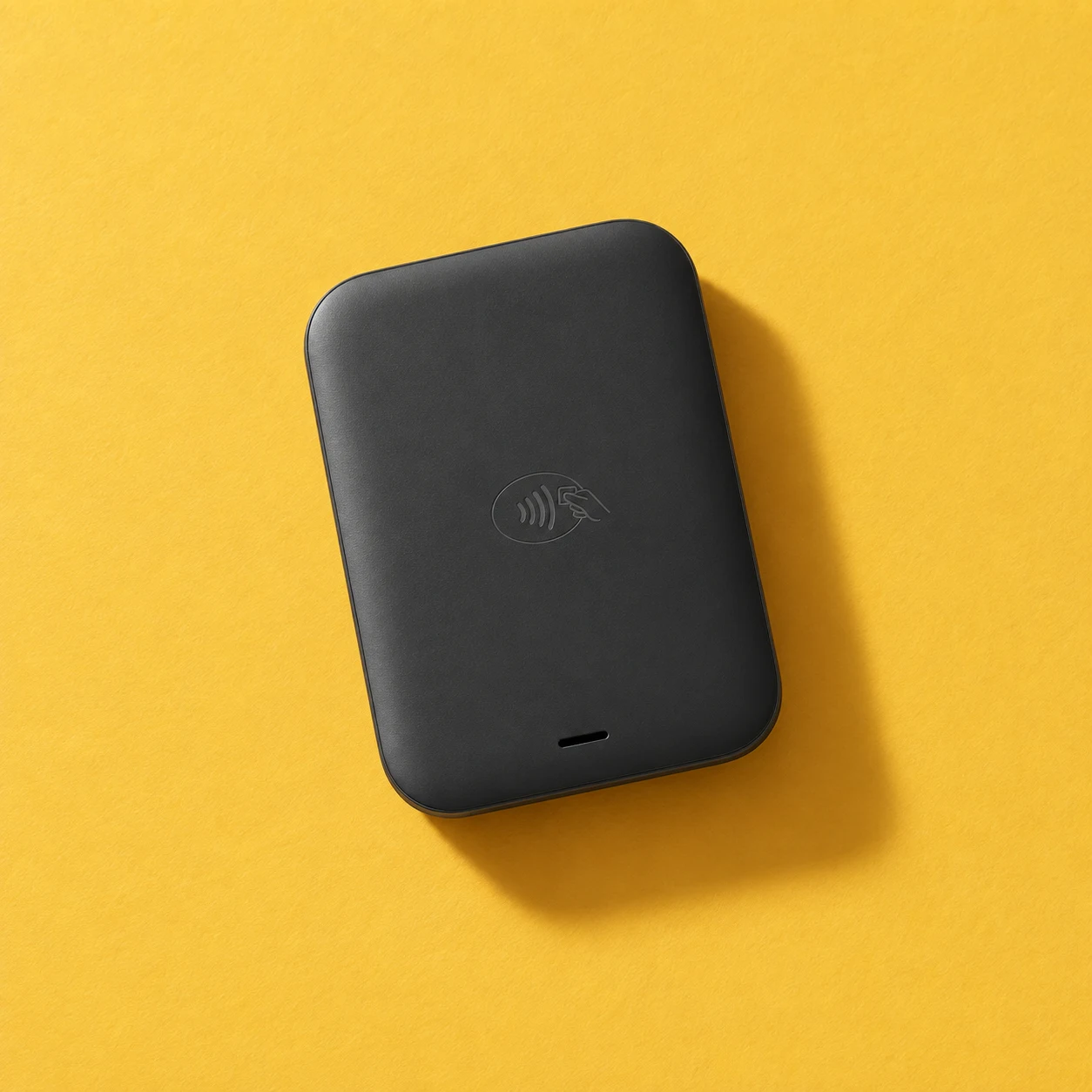 Illustrative overhead view of the compact black Comb Go reader on a warm yellow surface. No built-in screen.